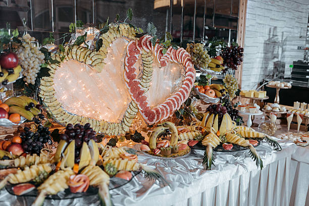 A table full of fruit and vegetables, including grapes, bananas, and apples. The table is decorated with a heart-shaped centerpiece made of fruit