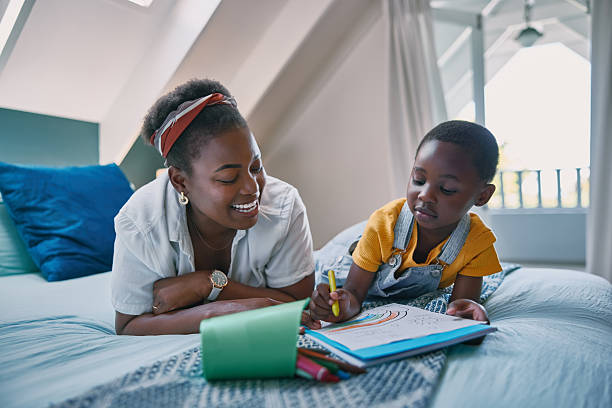 istock Mom, boy and coloring book on bed with learning, development and support with bonding in home. African woman, child and paper in bedroom with drawing, art and happy with education in family house 2210374849