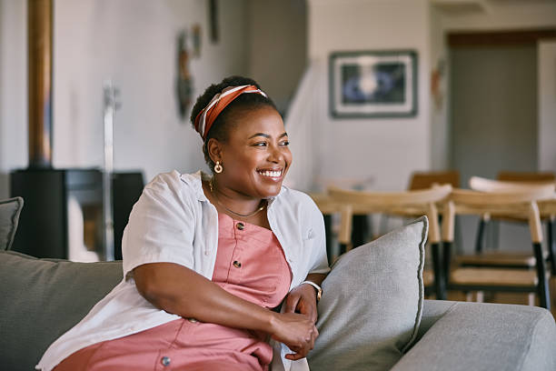 istock Black woman, relax and happy with thinking on sofa for reflection, daydreaming and remember memory. Person, smile and thoughtful in living room with weekend break, wondering and comfortable in home 2210374918