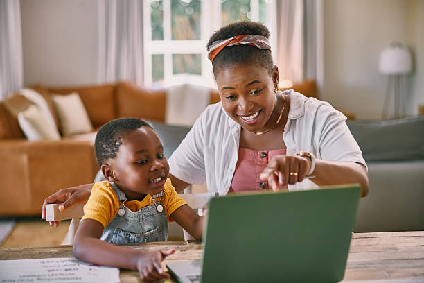 istock Mother, boy and laptop for e learning in home with point, help or education game for development. Black woman, child and computer for online course, happy or show for teaching on web at family house 2210374923