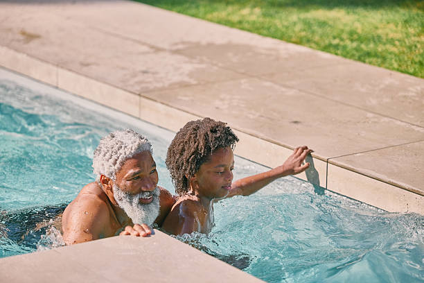 istock Swimming, pool and grandpa with child for playing, bonding and development together on weekend. Black family, summer and grandfather with boy in water for exercise, health and learning outdoor 2210374968