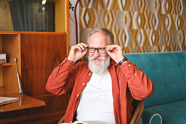 Portrait of a smiling senior man adjusting his eyeglasses while sitting in a chair at home