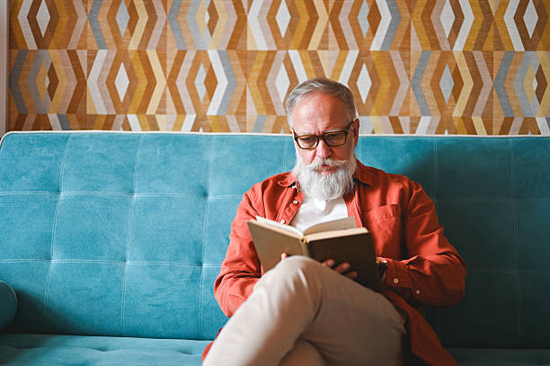 istock Senior man reading a book on the sofa at home 2210381718