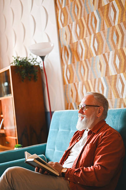 istock Senior man relaxing on sofa reading a book at home 2210381721