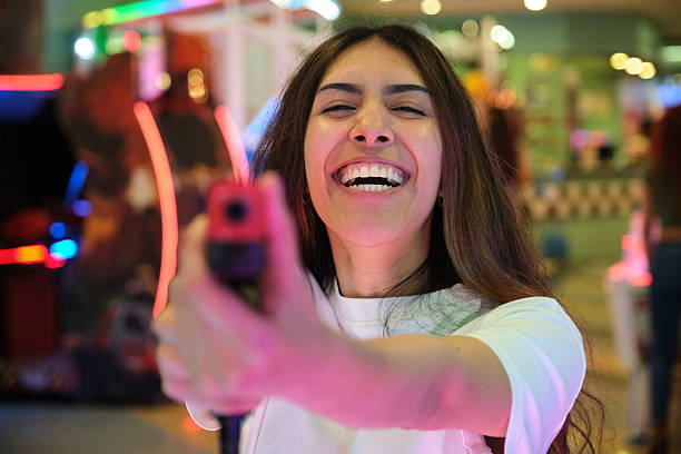 istock Young woman having fun playing arcade shooting game with light gun 2210383962