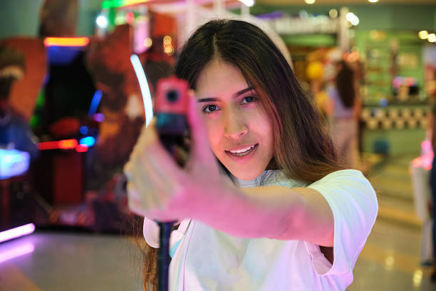 Young woman playing arcade shooting game with toy gun in amusement park