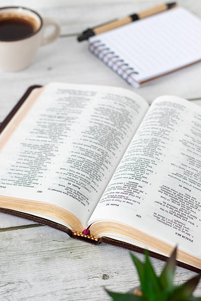 istock Open holy bible book with coffee cup and notebook on wooden desk 2210390177