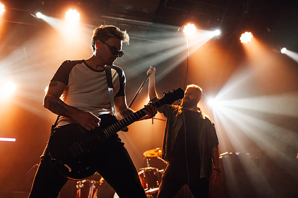 Rock band playing live on stage under orange lights, guitarist playing electric guitar and singer singing into microphone