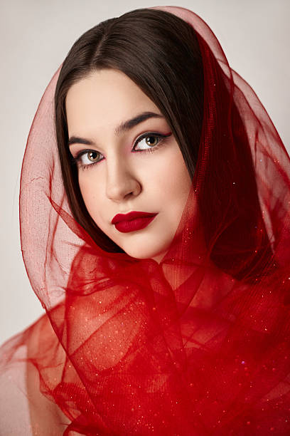 istock woman wears a flowing red sheer fabric that frames her face, accentuating her bold makeup with red lips and captivating eyes, showcasing a stunning beauty expression 2210391038