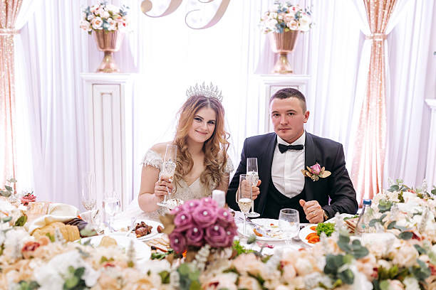 istock A bride and groom are sitting at a table with a white curtain behind them 2210391990