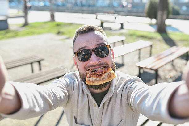 Goofy Male Looking at Camera While Biting Pizza Slice Making Silly Faces