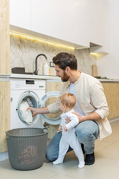 istock Young caucasian guy and his little son sorting clothes before putting into washing machine 2210393525