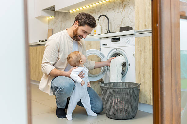istock Young caucasian guy and his little son sorting clothes before putting into washing machine 2210393526