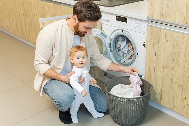 istock Young man and his little son sorting clothes before putting into washing machine 2210393536
