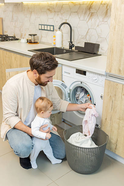 istock Young man and his little son sorting clothes before putting into washing machine 2210393542