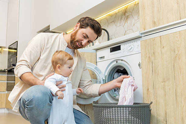 istock Young man and his little son sorting clothes before putting into washing machine 2210393550