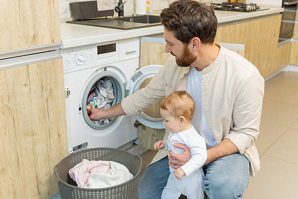 istock Young man and his little son sorting clothes before putting into washing machine 2210393551