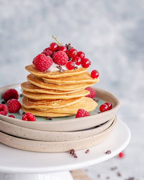 Stack of pancakes served with yoghurt, red berries and cacao nibs