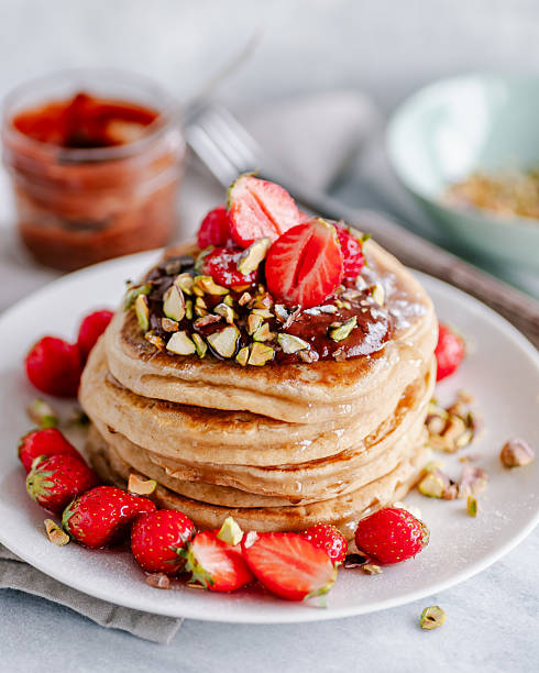 Stack of fluffy pancakes served with chocolate sauce, fresh strawberries, crushed pistacchios and syrup