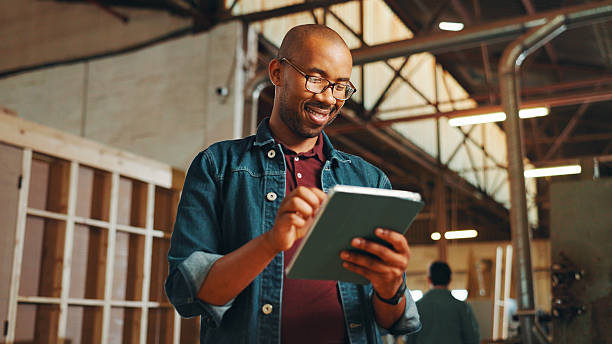 istock Carpentry, happy or man with tablet in workshop for inventory management, woodwork order or quality control. Timber manufacturing, black person and digital app for furniture production or client chat 2210394821