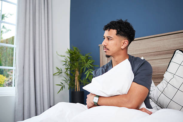 Young Man Sitting Thoughtfully on Bed in a Modern Bedroom Setting