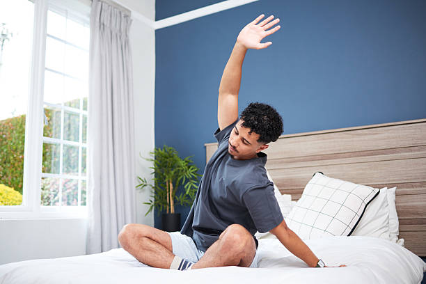 Person Practicing Morning Stretching Exercise on a Bed in a Sunlit Bedroom
