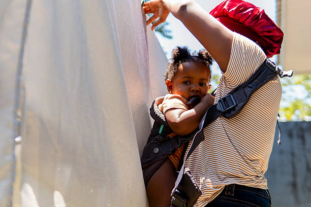 Mother hanging laundry on a clothesline outside while carrying her baby girl in a baby carrier