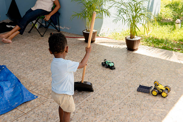 Young boy helps with chores by sweeping the patio while his mother relaxes nearby