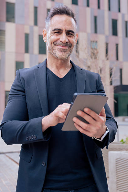 istock Businessman typing on tablet outdoors with modern building looking at camera 2210399067