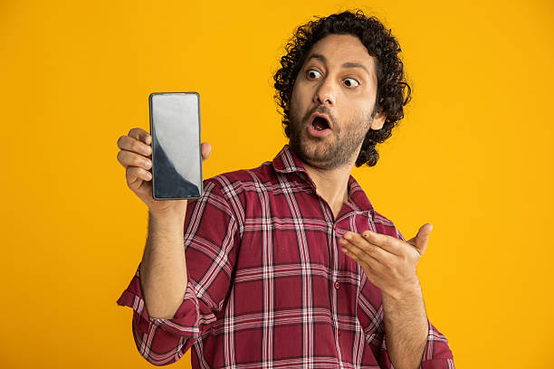 istock Surprised man showing smart phone on yellow background 2210404244