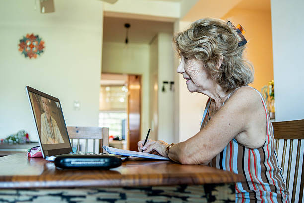 istock Senior woman making video call on laptop and taking notes at home 2210406896
