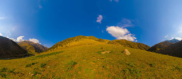 istock Wide panoramic view of a grassy mountain slope under a clear blue sky with scattered clouds. 2210409587