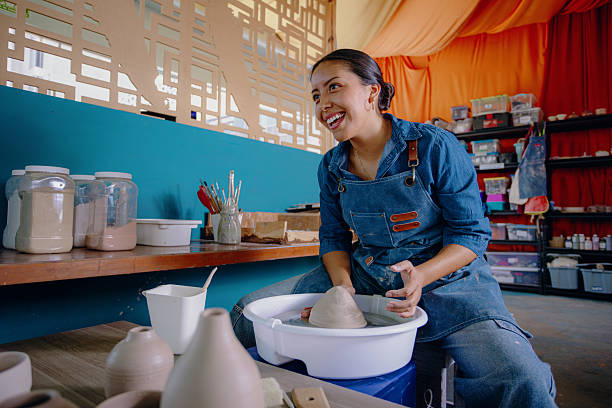 Young Mexican woman molding ceramics in her blue workshop attire