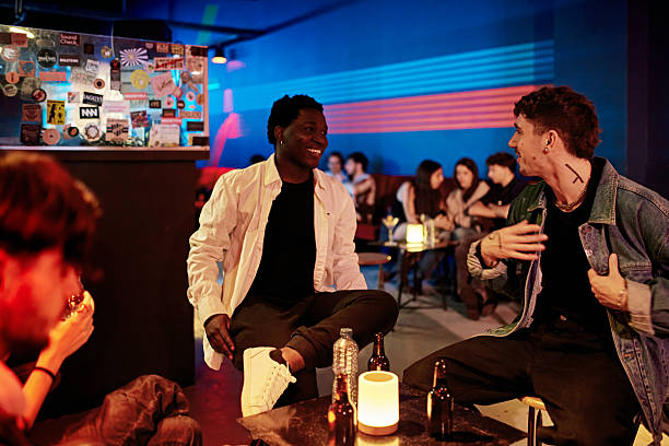 Casually dressed friends sitting at small table, face to face, interacting and laughing, enjoying relaxed leisure time after work.