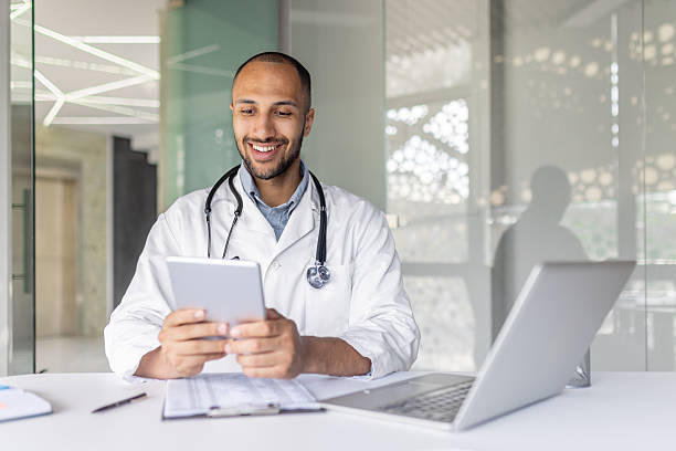 istock Successful experienced doctor sitting at desk inside the clinic office and using a tablet computer. Man in a white medical coat, using an application for online communication and consulting patients 2210423685