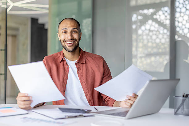 istock Portrait joyful successful financier, man with documents and financial reports in his hands smiles and looks at the camera. Businessman works inside the office with bills, satisfied with the results 2210425920