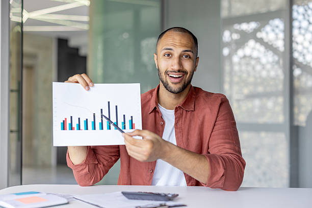 istock Successful man with document, graph, report looking at camera, showing colleagues and partners successful results of achievement, using video meeting, online call, working inside office 2210425921