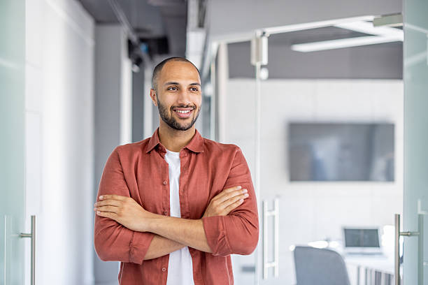 istock Young businessman smiles confidently while standing with arms crossed in a modern office environment, exuding professionalism. 2210425965