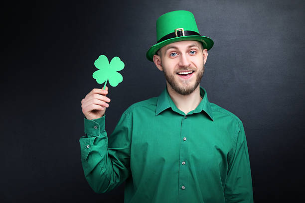 St. Patrick's Day. Young man wearing green hat with paper clover on black background