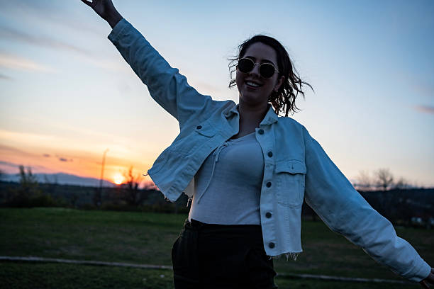 Happy teenage girl whit her eyes closed raising her hands on a hill during sunset