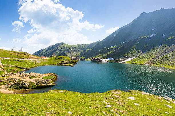 balea lake of romania balea lake of romania. alpine landscape of fagaras mountains with pond. sunny weather with clouds on the blue sky above carpathians. snow and grass on the hillside in summer. idyllic place balea lake romania stock pictures, royalty-free photos & images