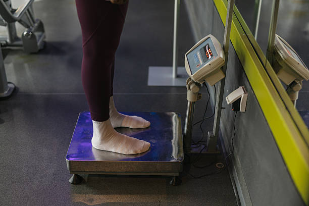 A person standing barefoot on a scale in a gym environment, indicating a moment of self-reflection during their fitness journey to measure weight and progress.