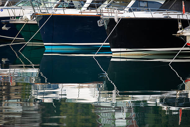 Various yachts and boats moored at a pier on the Bosphorus in Istanbul. Their reflections are clearly visible on the calm water. In the foreground, the edge of a small boat and a few seagulls on the surface. On the opposite side, hillside residential areas appear in a hazy silhouette.