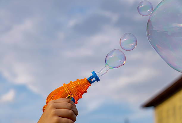 istock child holding a bubble gun, blowing colorful bubbles against the sky 2210438344