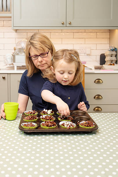 istock Cheeky 4 year old girl decorating her chocolate corn flake Easter nests while sitting on her grandmothers lap in a domestic kitchen 2210440967