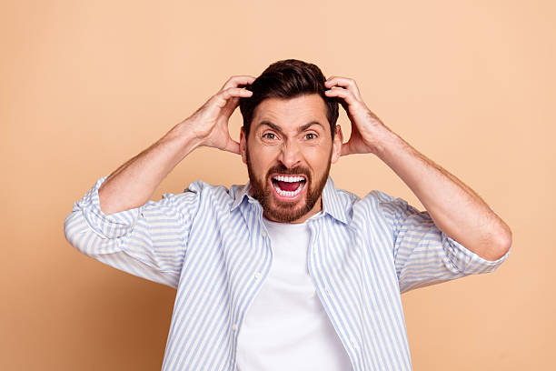 istock Frustrated young man gripping his hair with a loud shouting expression against a plain beige background 2210441161