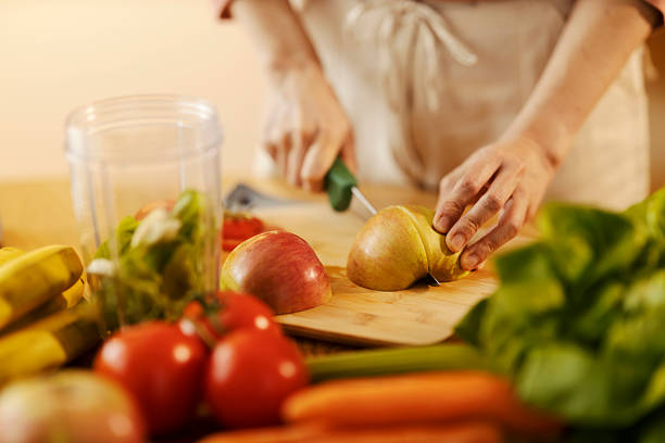 Cropped picture of female's hands cutting apple in kitchen on cutting board.