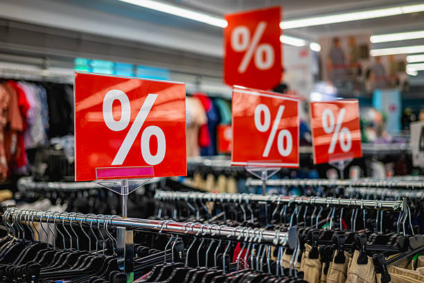 istock Red discount signs hanging in clothing store interior during sale, shopping season. Generic discount sale sign of shop. Retail Promotion, Discount Concept 2210453473