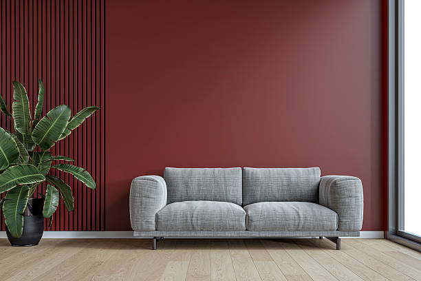 istock A modern minimalist interior with a gray textile sofa, a potted plant in front of an empty dark deep red plaster, partly dark deep red paneled wall background with copy space, a large window by one side 2210459730