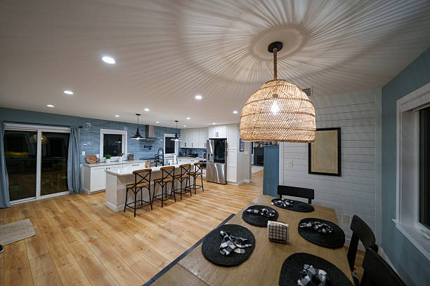 Wide shot of a modern farmhouse style dining area and kitchen with stainless steel appliances, kitchen island, white cabinetry, and blue tile backsplash in a middle-class home in Maryland, USA.
